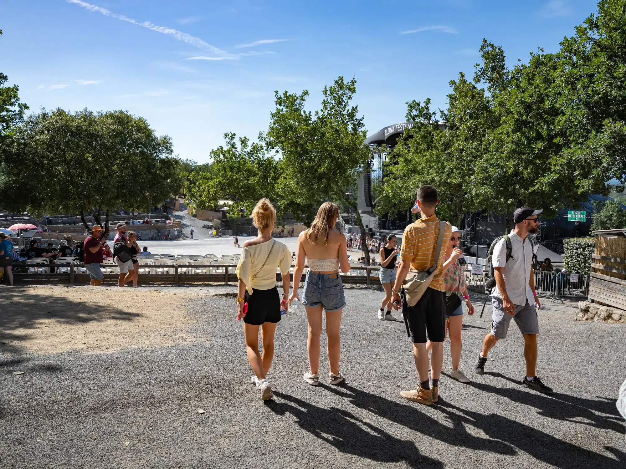 Public marchant sur un chemin en gravier vers une scène de festival en plein air.
